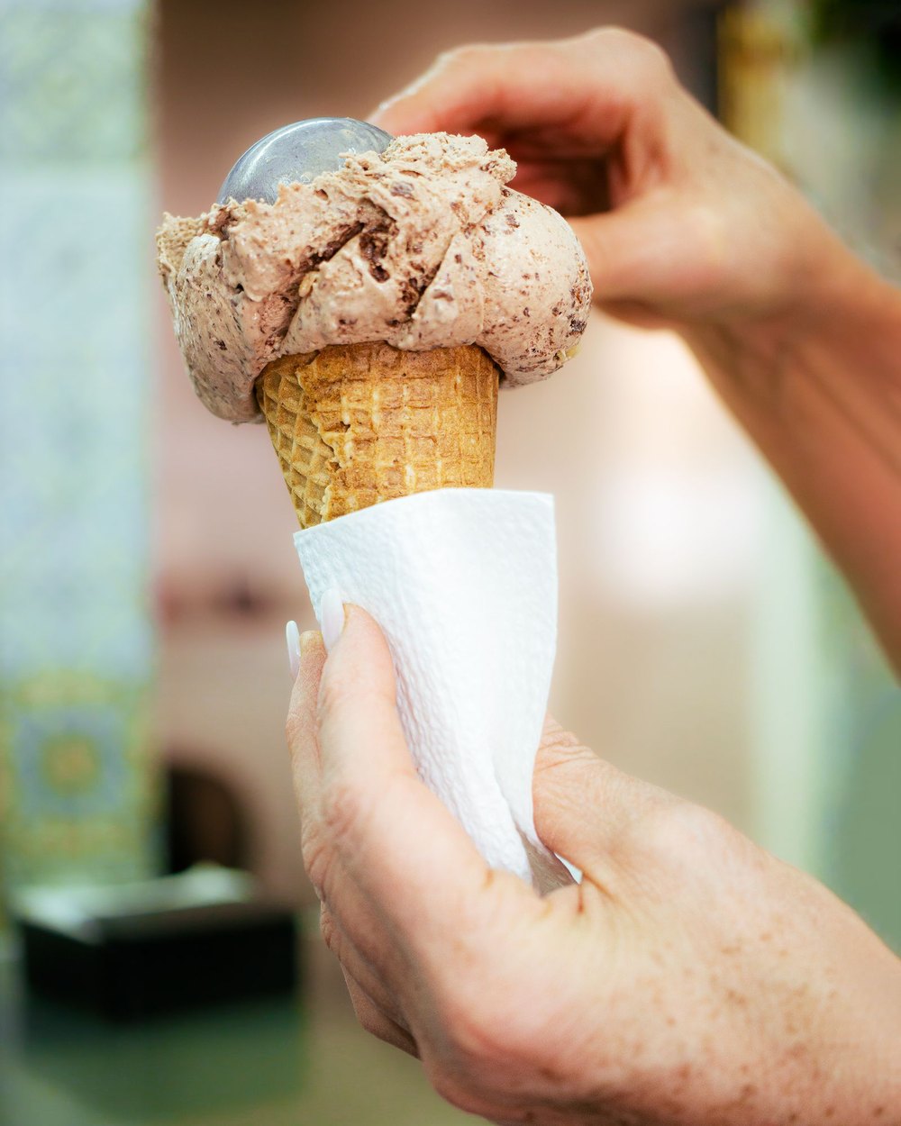 A cone of ice cream passed across a counter, wrapped in a paper napkin.