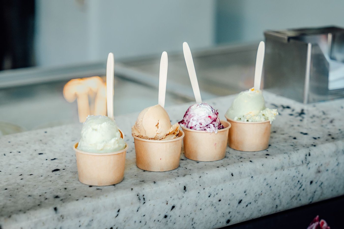 Four small cups of ice cream lined up on a speckled stone counter.