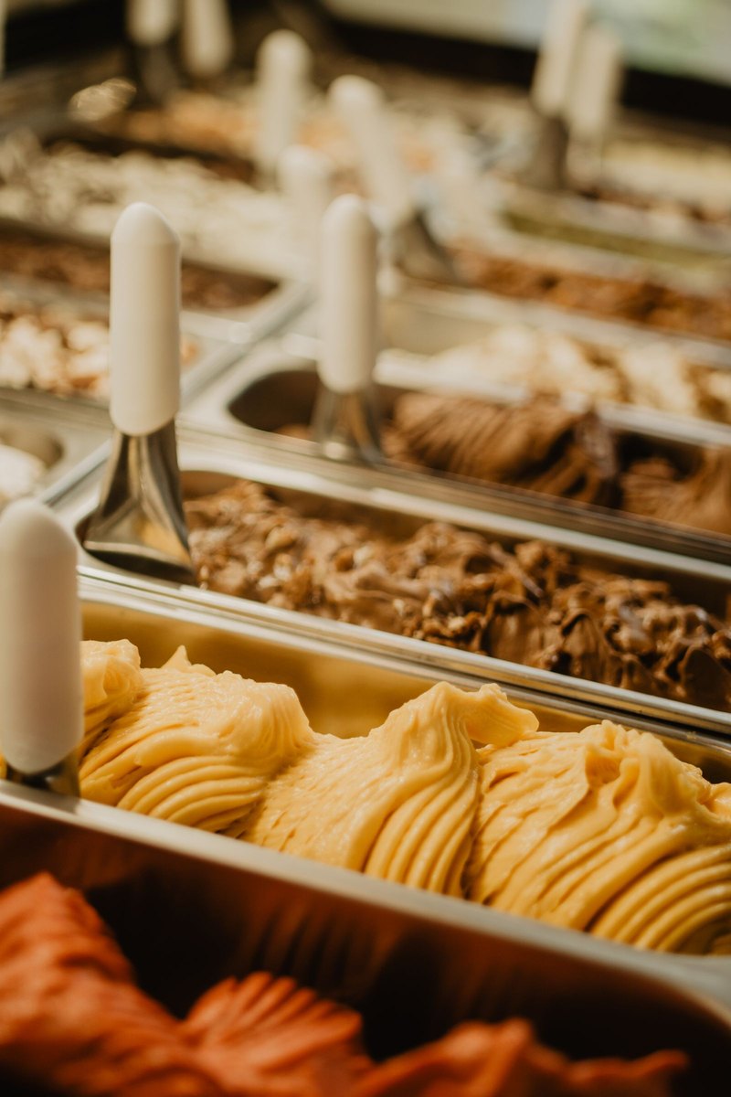 Trays of freshly piped ice cream in a shop freezer, warm cream and caramel tones.